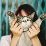 A woman playfully holds her tabby cat with paws up, creating a charming pet portrait.